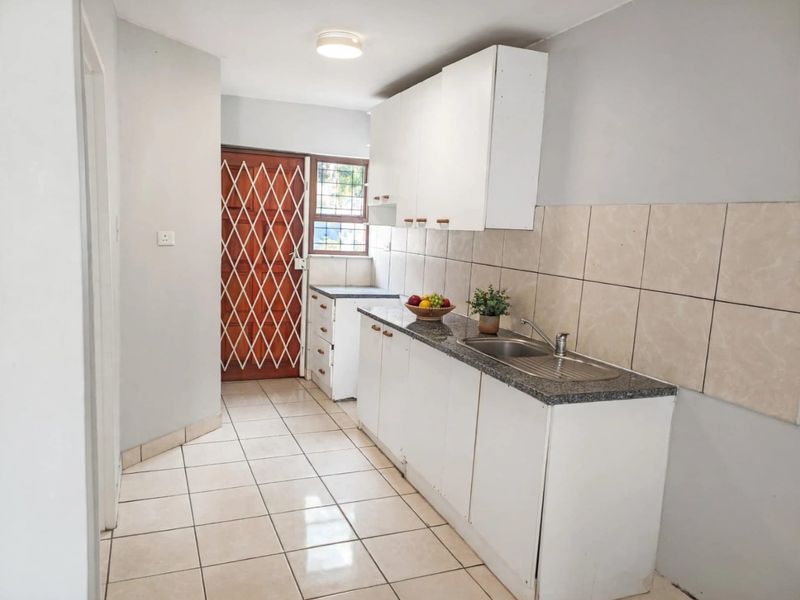 A functional kitchen featuring white cabinetry, granite countertops, a stainless steel sink, tiled backsplash, and tiled flooring with direct access to an exterior door.