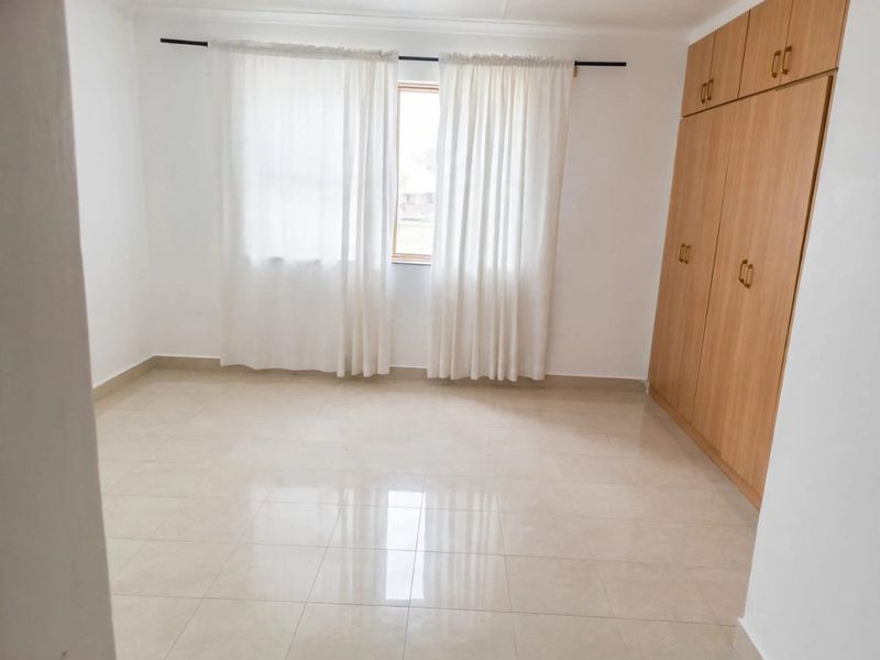A bright, empty bedroom featuring neutral tiled flooring and ample built-in wooden cupboards.