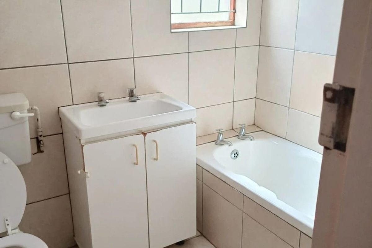 A functional bathroom featuring tiled walls and flooring, a built-in bathtub, and a vanity basin with storage cabinet.