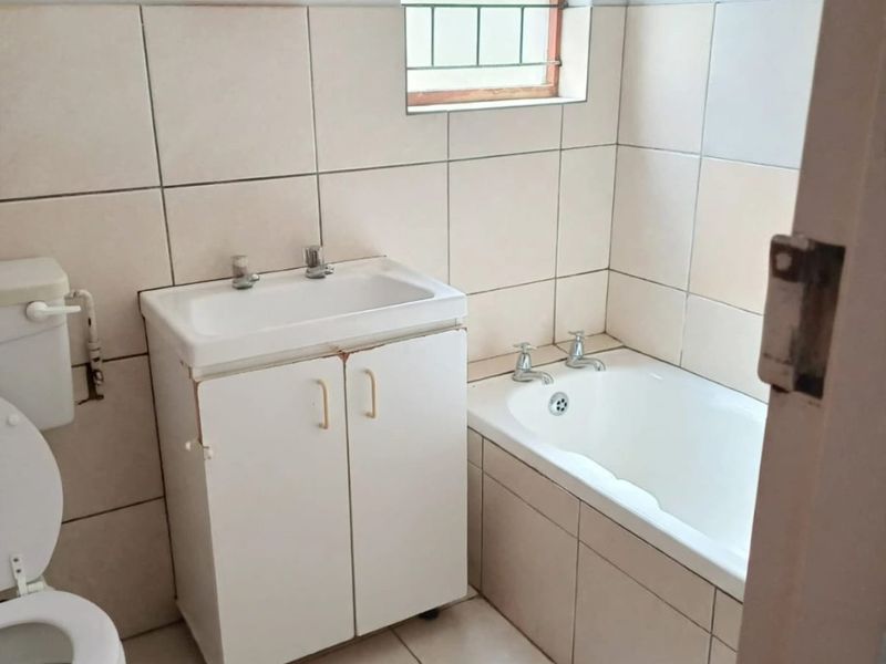 A functional bathroom featuring tiled walls and flooring, a built-in bathtub, and a vanity basin with storage cabinet.