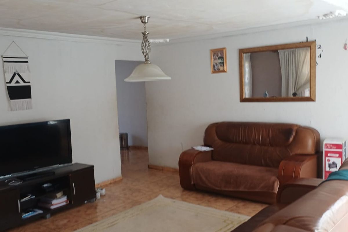 A living room featuring tiled flooring and a central pendant light fixture, showing signs of ceiling water damage and wear.