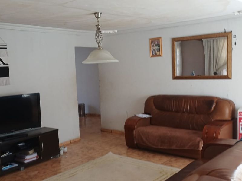 A living room featuring tiled flooring and a central pendant light fixture, showing signs of ceiling water damage and wear.