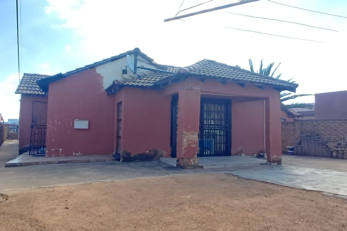Rear view of a detached house featuring a tiled roof, concrete patio area, and brick boundary walls, showing signs of exterior wear.