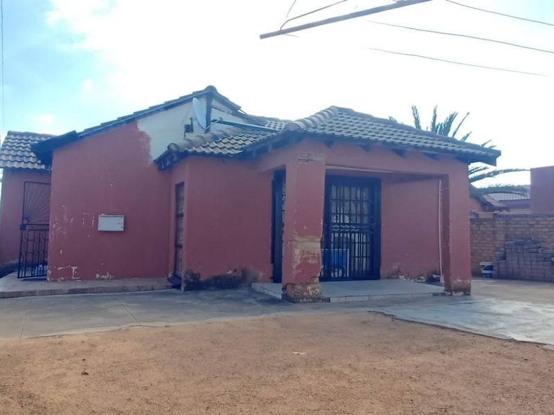 Rear view of a detached house featuring a tiled roof, concrete patio area, and brick boundary walls, showing signs of exterior wear.