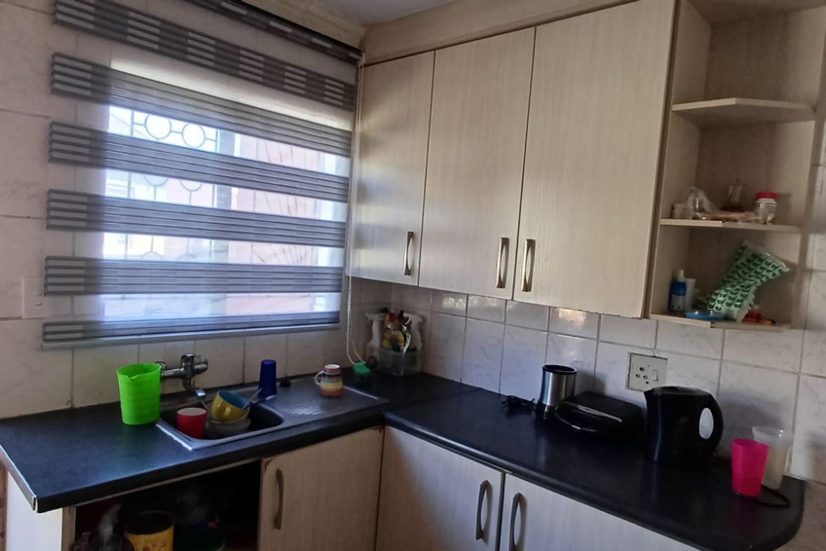 A compact kitchen featuring laminate cabinetry, dark countertops, a stainless steel sink, and tiled splashbacks with direct access to an outdoor area.
