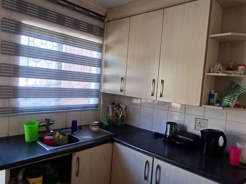 A compact kitchen featuring laminate cabinetry, dark countertops, a stainless steel sink, and tiled splashbacks with direct access to an outdoor area.