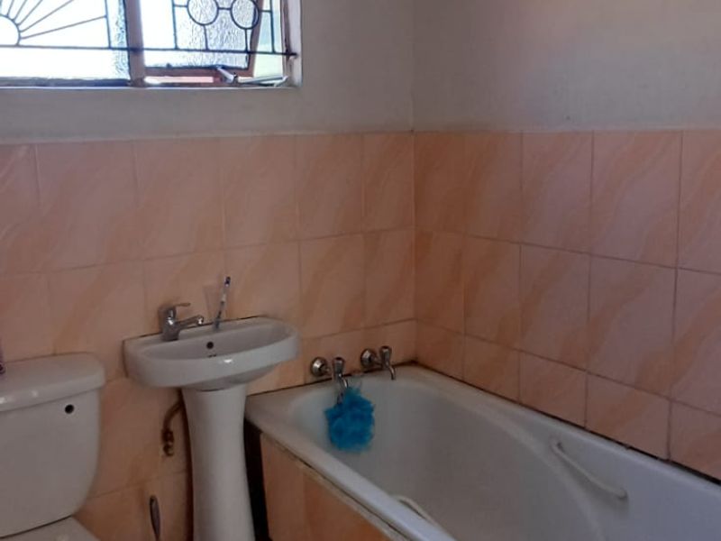A functional bathroom featuring a pedestal basin, bathtub, and toilet with dated wall and floor tiling.