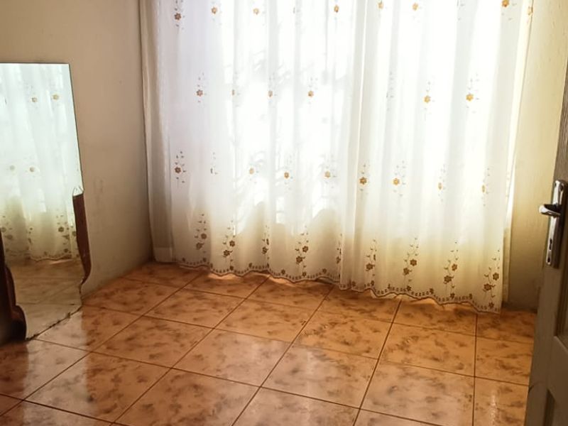 An empty bedroom featuring ceramic floor tiles, a ceiling rose, and decorative cornice, offering a blank canvas for renovation.