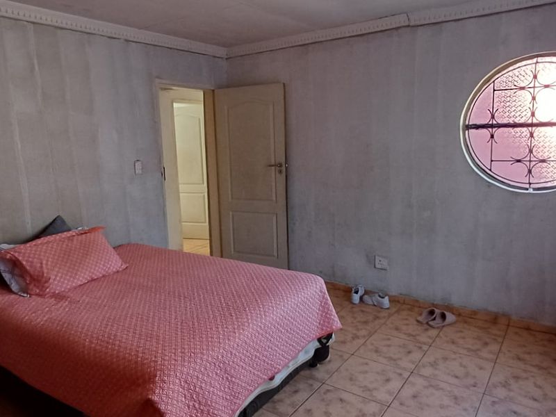 A bedroom featuring a distinctive circular window with security bars, tiled flooring, and unfinished wall surfaces requiring cosmetic attention.