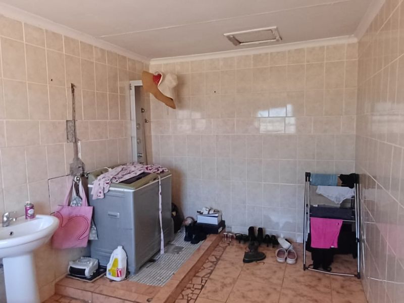 A functional laundry area featuring fully tiled walls, a pedestal basin, and tiled flooring, requiring some maintenance and cosmetic updates.
