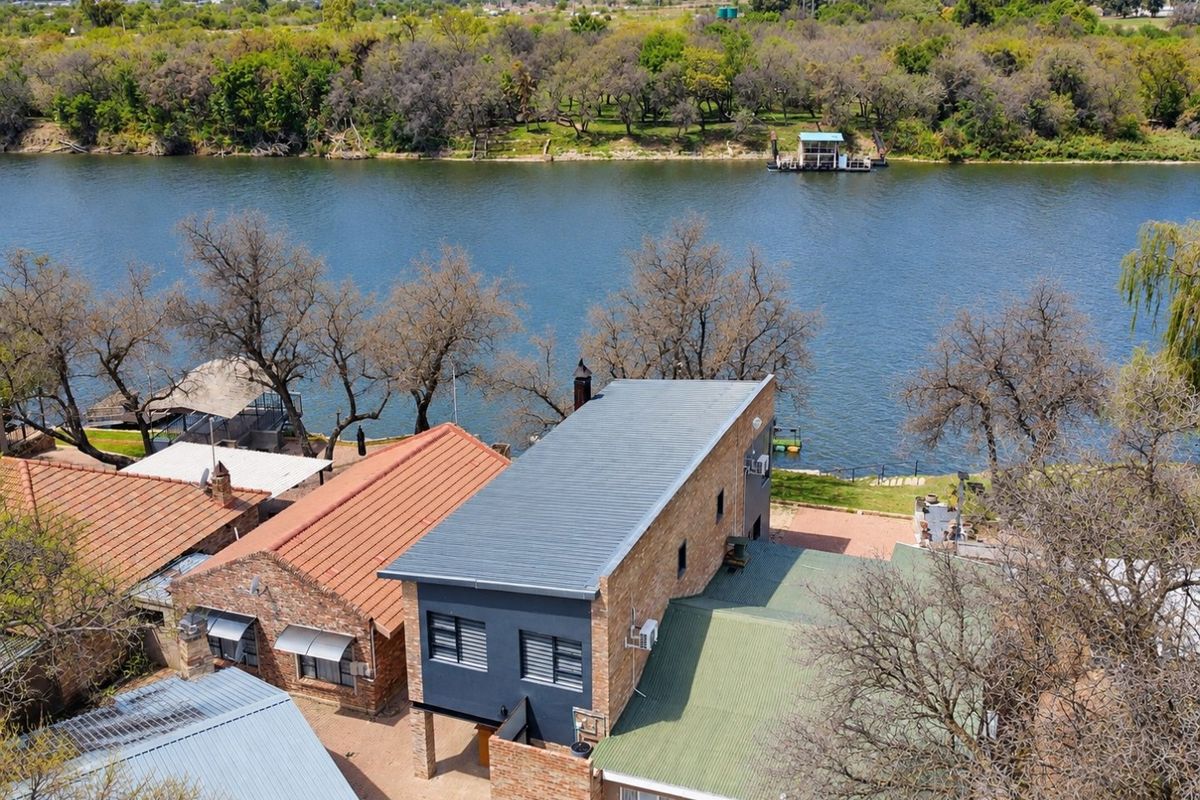 Aerial view of a multi-structure residential property featuring river frontage, metal roofing, and brick exterior finishes.