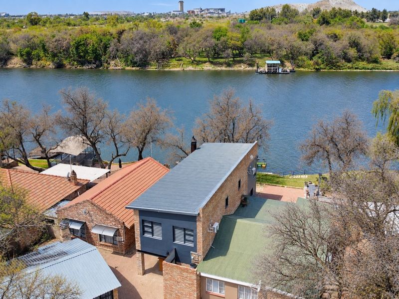 Aerial view of a multi-structure residential property featuring river frontage, metal roofing, and brick exterior finishes.