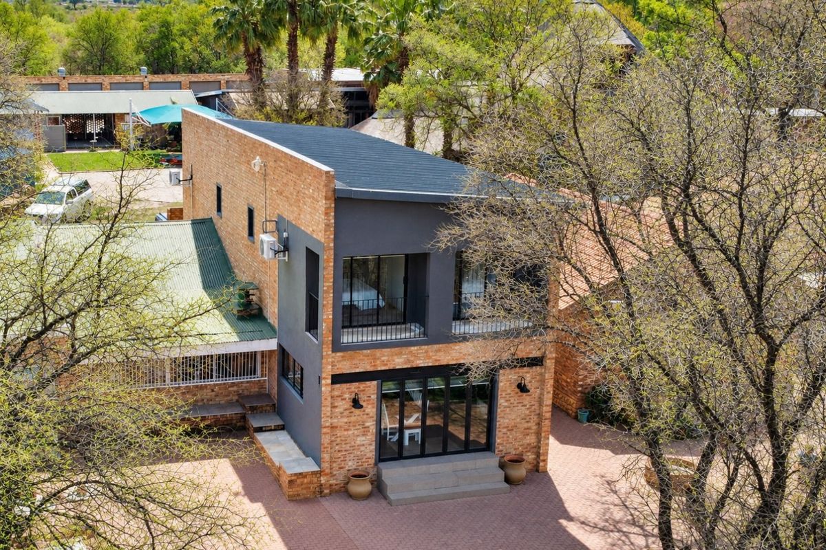 Aerial view of a modern two-story face brick residence featuring a balcony, black aluminium framed doors and windows, and a paved rear courtyard area.