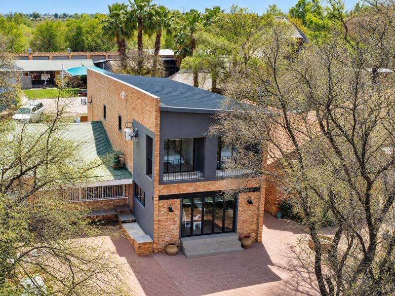 Aerial view of a modern two-story face brick residence featuring a balcony, black aluminium framed doors and windows, and a paved rear courtyard area.