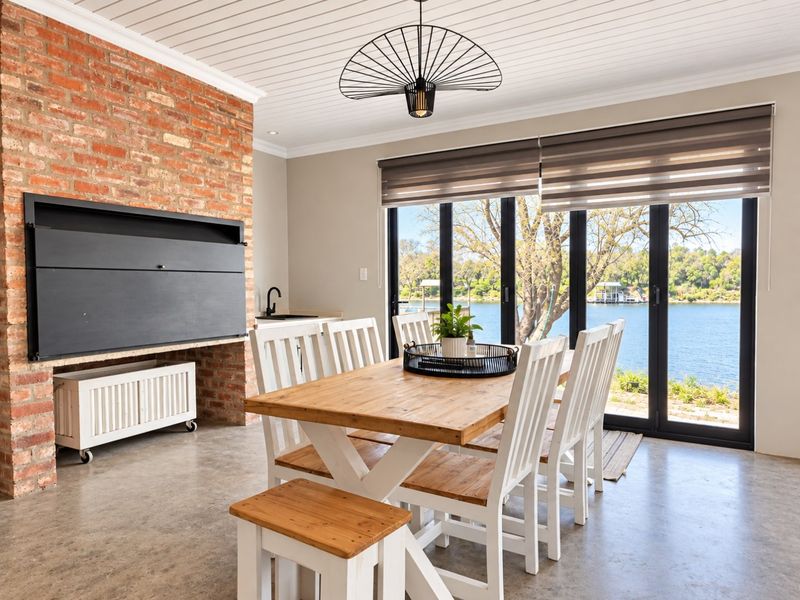 Bright dining area featuring exposed brickwork, a built-in fireplace, polished concrete floors, and large bi-fold doors opening to scenic waterfront views.