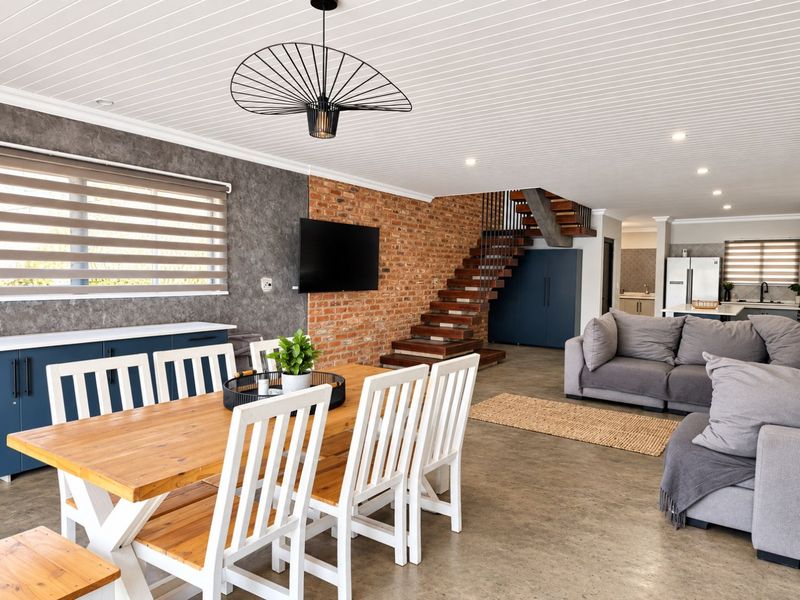 Spacious open-plan living and dining area featuring exposed brickwork, a modern timber staircase, polished concrete floors, and a contemporary tongue and groove ceiling.