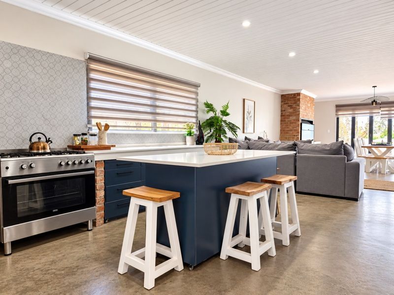 Spacious open-plan kitchen and living area featuring a central island, gas stove, exposed brick fireplace, and polished concrete flooring with modern finishes.
