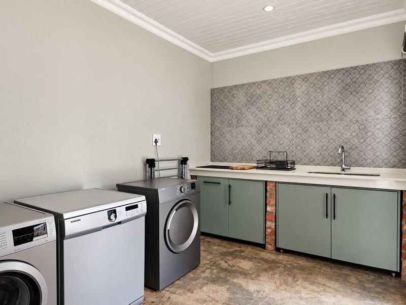 A well-appointed laundry room featuring built-in cabinetry, a sink, decorative tiled backsplash, and durable concrete flooring with exposed brick detailing.