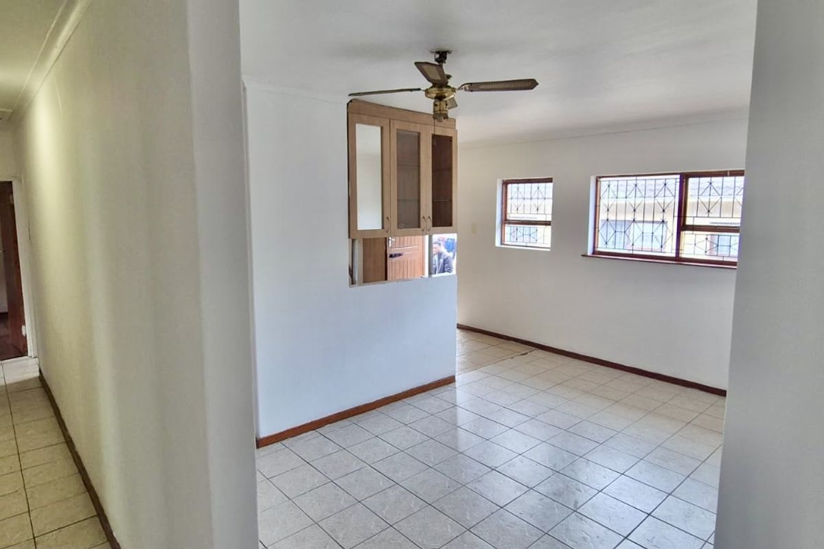 An empty living area featuring tiled flooring, a ceiling fan, and security bars on the windows, with a view into an adjacent hallway.