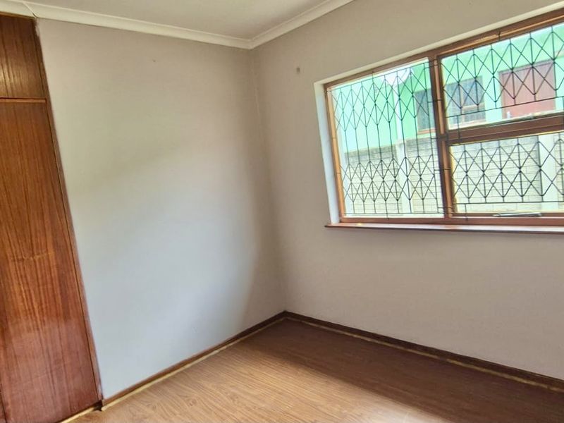 An empty bedroom featuring built-in wooden cupboards, laminate flooring, and a window fitted with security bars.