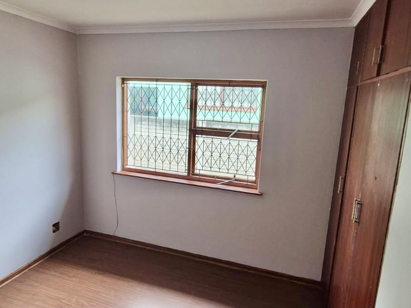 A vacant bedroom featuring laminate flooring, built-in wooden cupboards, and a window fitted with security bars.