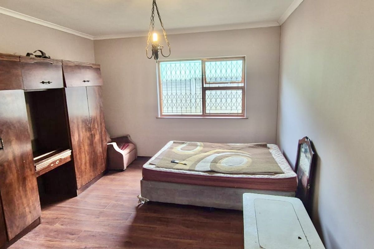 A bedroom featuring built-in wooden cupboards, laminate flooring, and a window fitted with security bars.