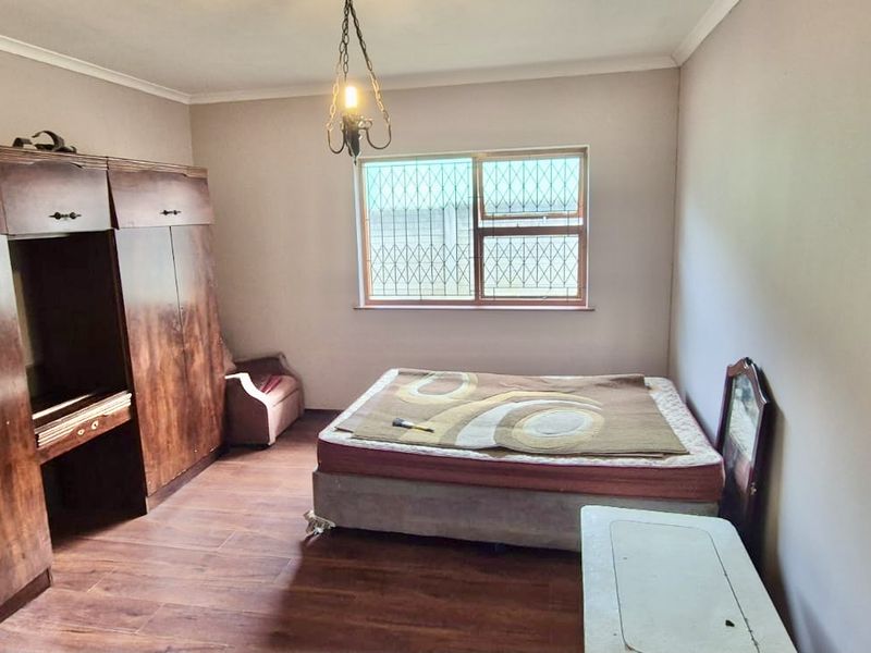 A bedroom featuring built-in wooden cupboards, laminate flooring, and a window fitted with security bars.