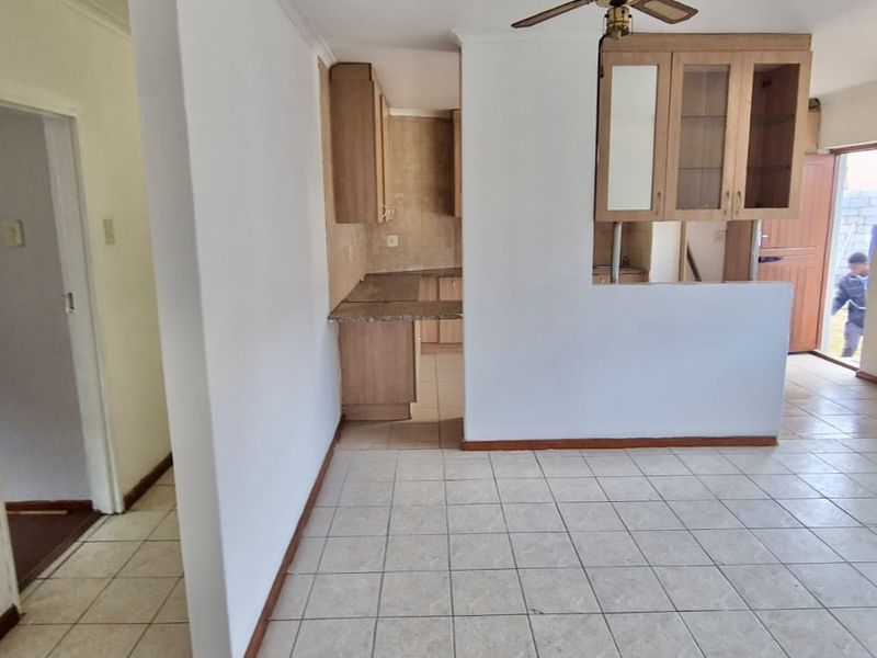 An open-plan living and kitchen area featuring tiled flooring, built-in cabinetry with granite countertops, and a ceiling fan.