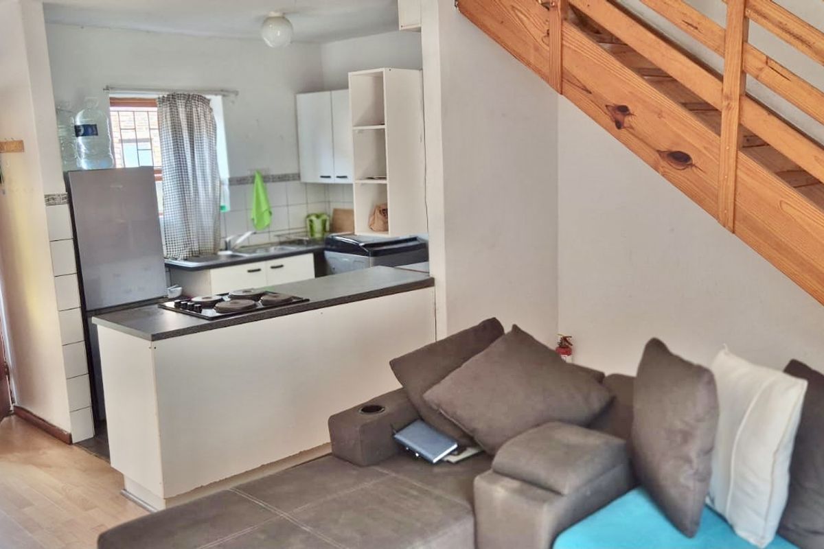 Open-plan living area featuring a compact kitchen with built-in cabinetry and a wooden staircase leading to the upper level.