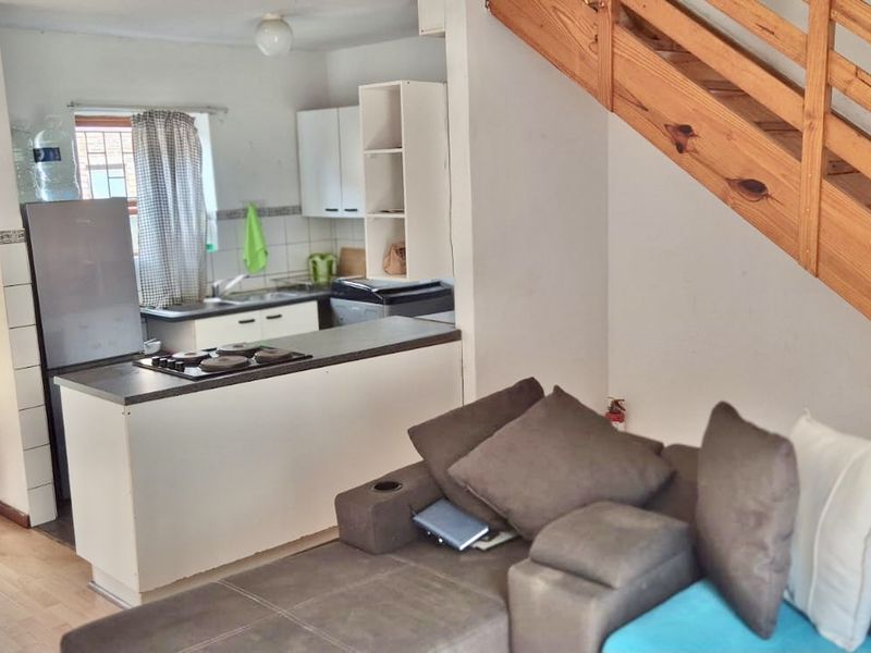 Open-plan living area featuring a compact kitchen with built-in cabinetry and a wooden staircase leading to the upper level.