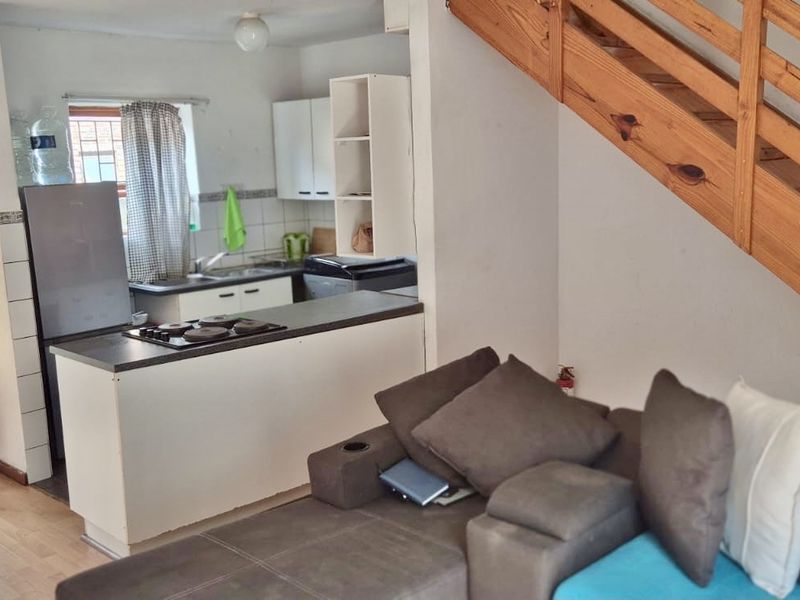Open plan living area featuring a compact kitchen with built-in hob and a wooden staircase leading to the upper level.
