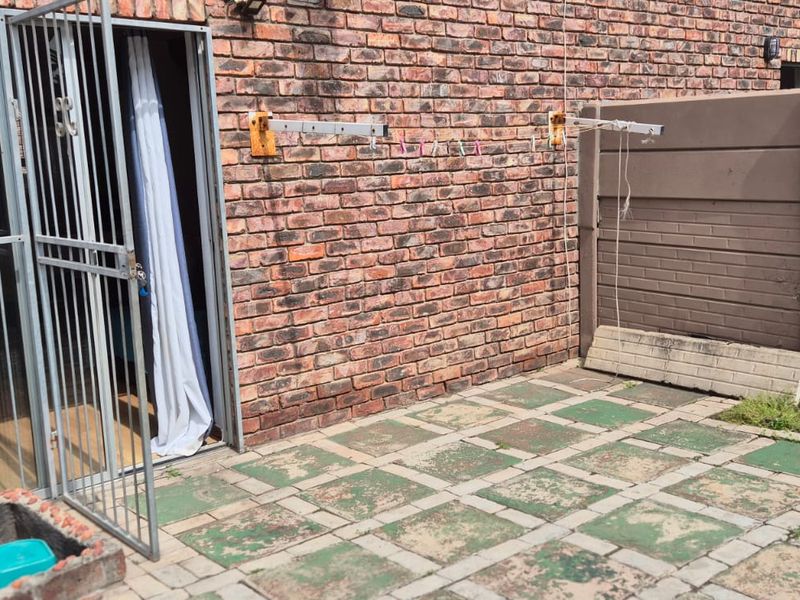A rear courtyard area featuring a brick facade, paved patio space, security gate, and wall-mounted clothesline, offering potential for outdoor improvement.