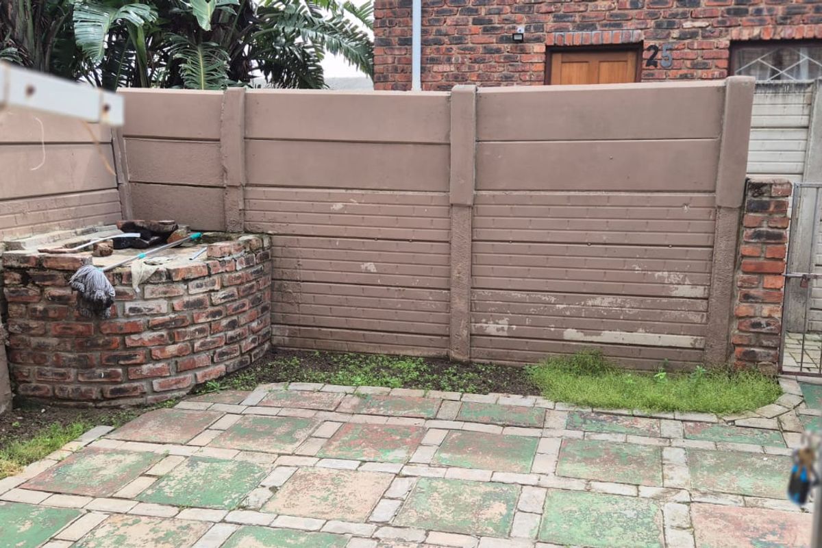 A private rear courtyard featuring a brick built-in braai, paved patio area, and precast concrete boundary walls in need of maintenance.