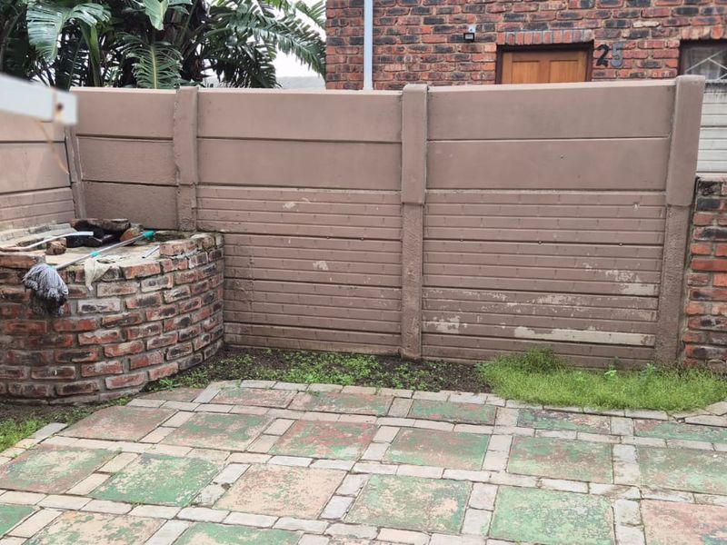 A private rear courtyard featuring a brick built-in braai, paved patio area, and precast concrete boundary walls in need of maintenance.