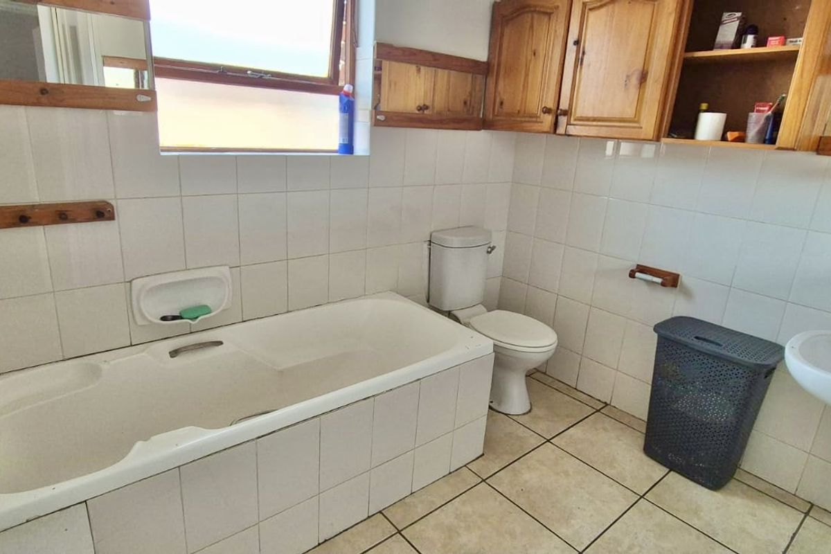 A dated bathroom featuring a tiled bathtub, wall-mounted basin, toilet, and wooden cabinetry, requiring modernization to improve its aesthetic and functionality.