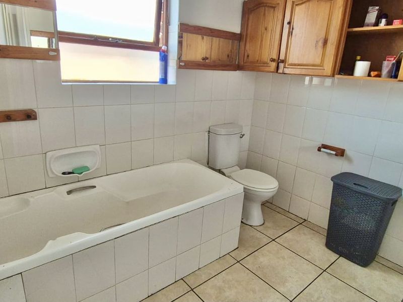 A dated bathroom featuring a tiled bathtub, wall-mounted basin, toilet, and wooden cabinetry, requiring modernization to improve its aesthetic and functionality.