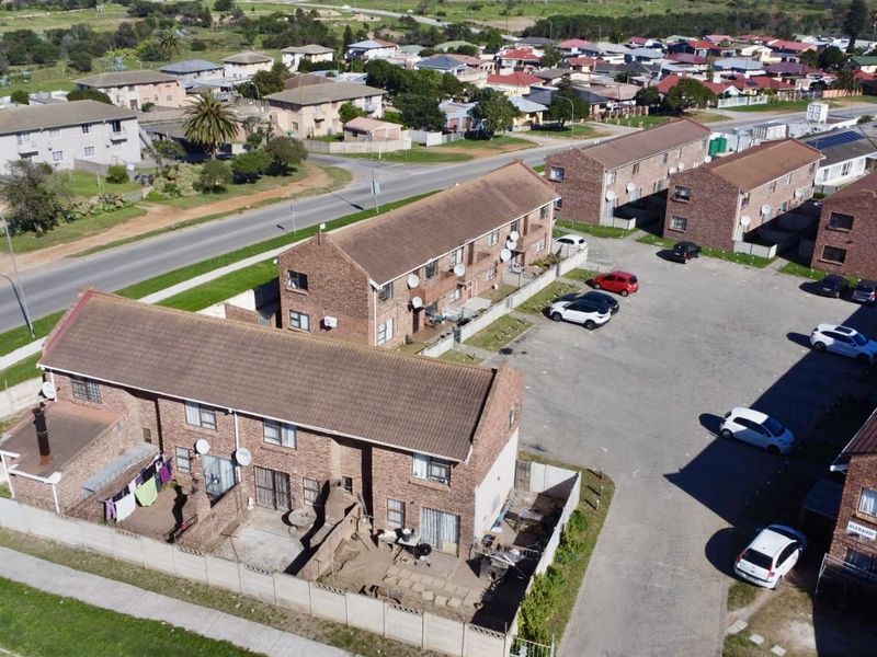 Aerial view of a townhouse complex featuring brick buildings, tiled roofs, and a shared paved parking area within a residential neighborhood.