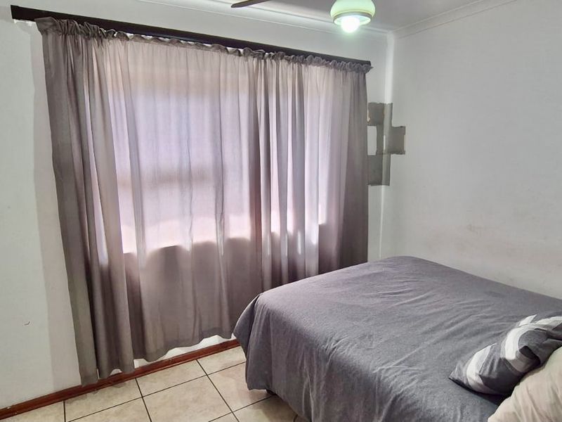 A functional bedroom featuring tiled flooring, a built-in wardrobe, and a ceiling fan, offering a neutral base for personalization.