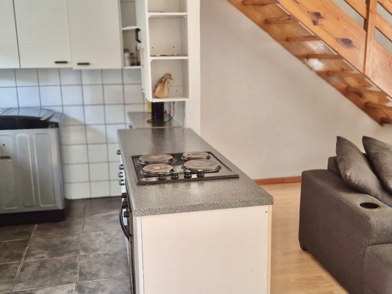 Open plan kitchen featuring built-in cabinetry, electric hob, and tiled splashback, adjacent to a living area with a wooden staircase.