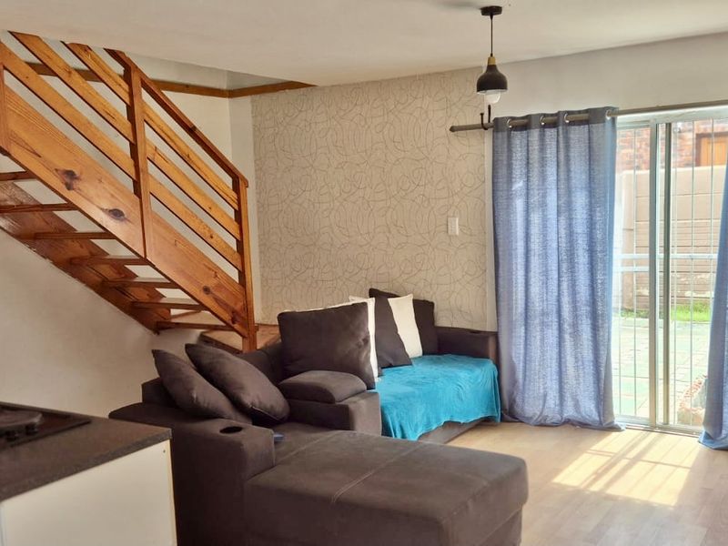 Open-plan living area featuring a wooden staircase, built-in kitchen hob, and sliding glass doors leading to the exterior.