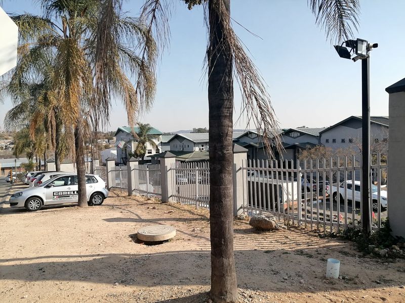 Exterior view of the commercial property frontage featuring metal security fencing, security lighting, and a paved driveway area.