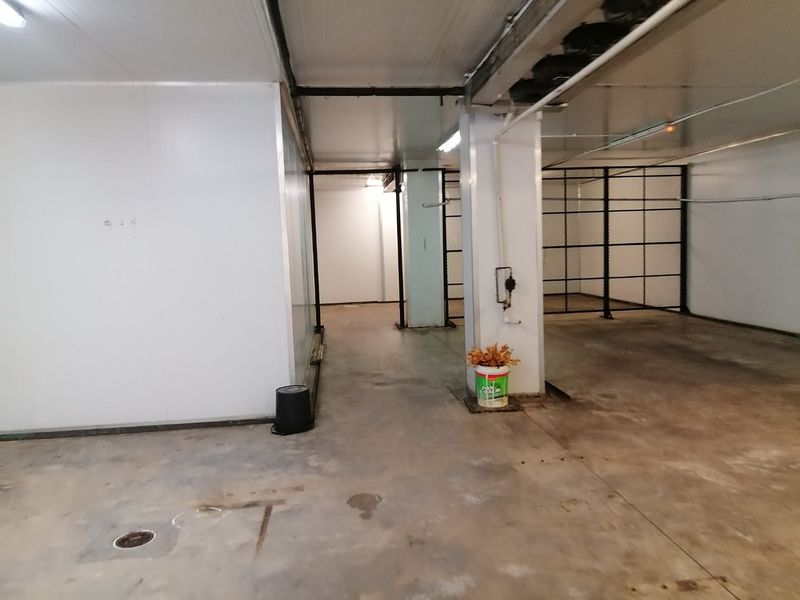 A functional utility or storage space featuring concrete flooring, metal partition fencing, and exposed ceiling infrastructure, suitable for industrial or commercial storage use.