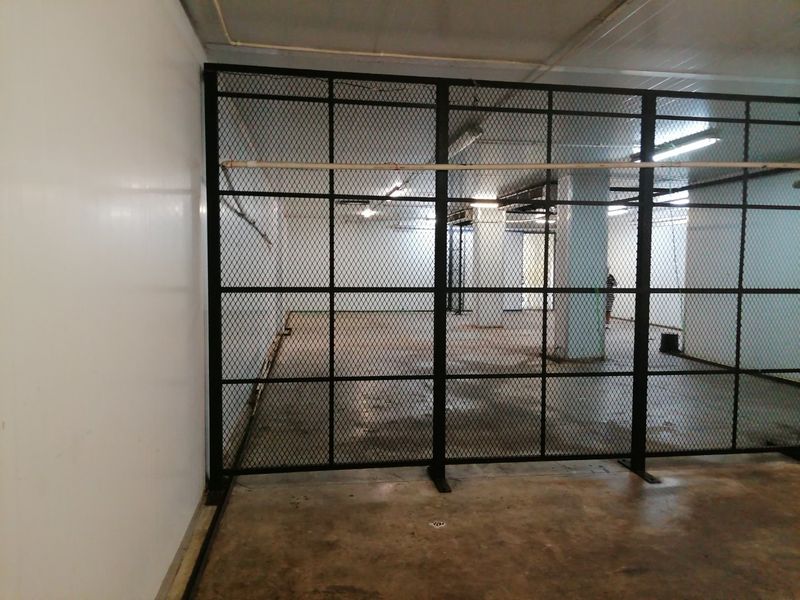A secure utility or storage area featuring a metal mesh partition, exposed ceiling infrastructure, and durable concrete flooring.
