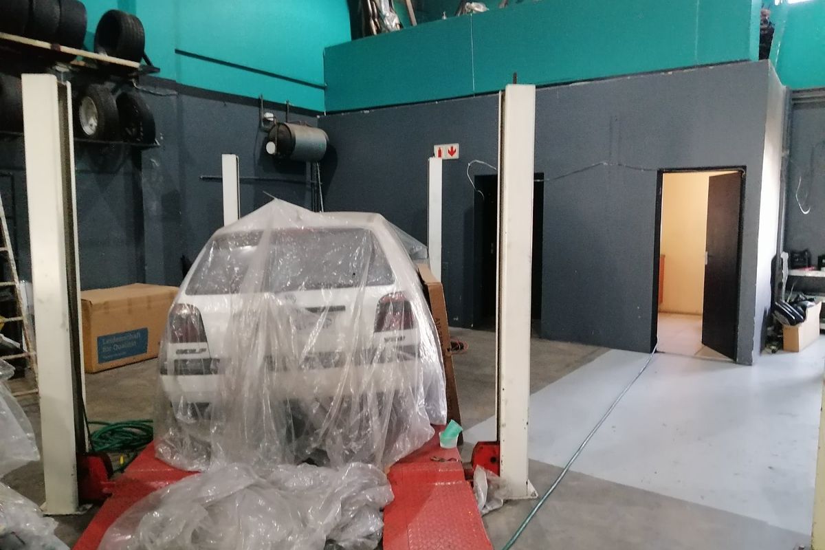 Commercial garage space featuring a two-post vehicle lift, mezzanine level, and painted concrete flooring, suitable for automotive workshop operations.