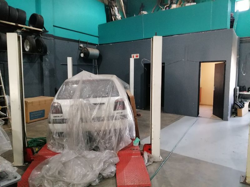 Commercial garage space featuring a two-post vehicle lift, mezzanine level, and painted concrete flooring, suitable for automotive workshop operations.