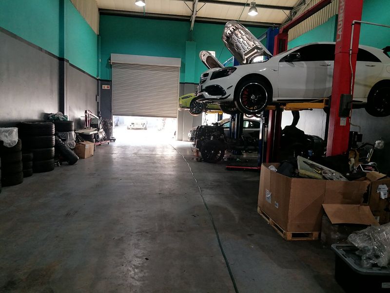 Commercial garage workshop featuring a high-clearance roller shutter door, concrete flooring, and a built-in vehicle hydraulic lift system.