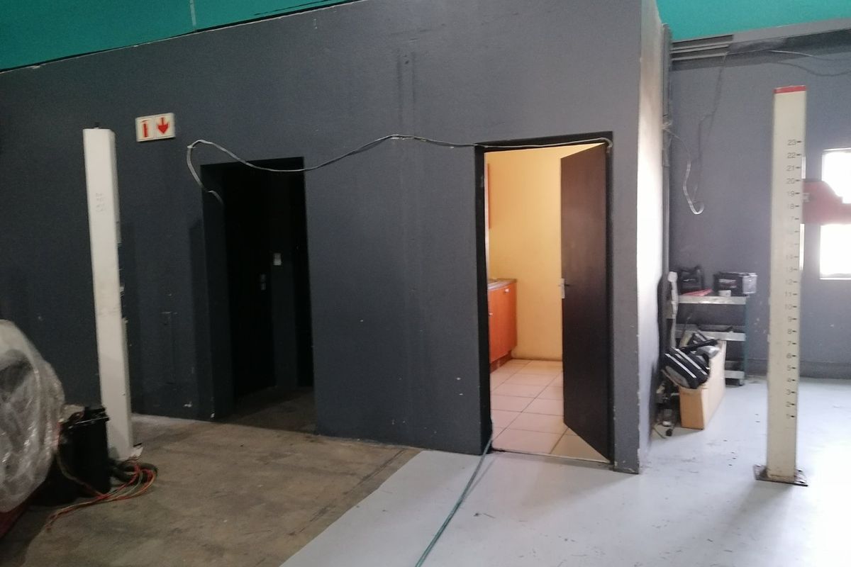 A utilitarian commercial space featuring painted concrete flooring, exposed wiring, and multiple internal access points, suitable for workshop or storage use.