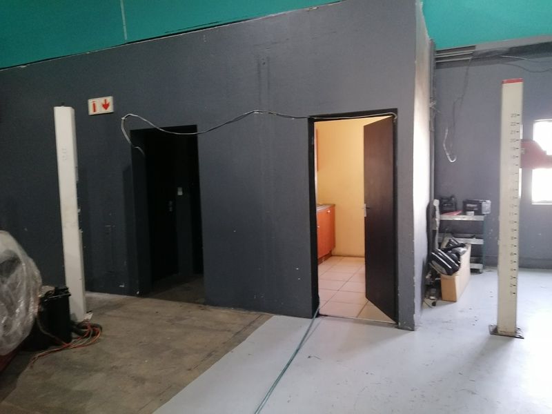 A utilitarian commercial space featuring painted concrete flooring, exposed wiring, and multiple internal access points, suitable for workshop or storage use.