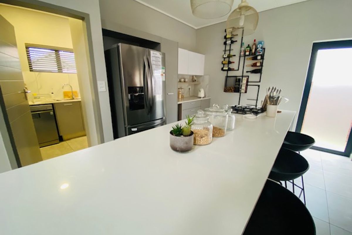Modern kitchen featuring a large central island with quartz countertops, sleek cabinetry, and integrated appliances, with convenient access to an adjoining scullery area.
