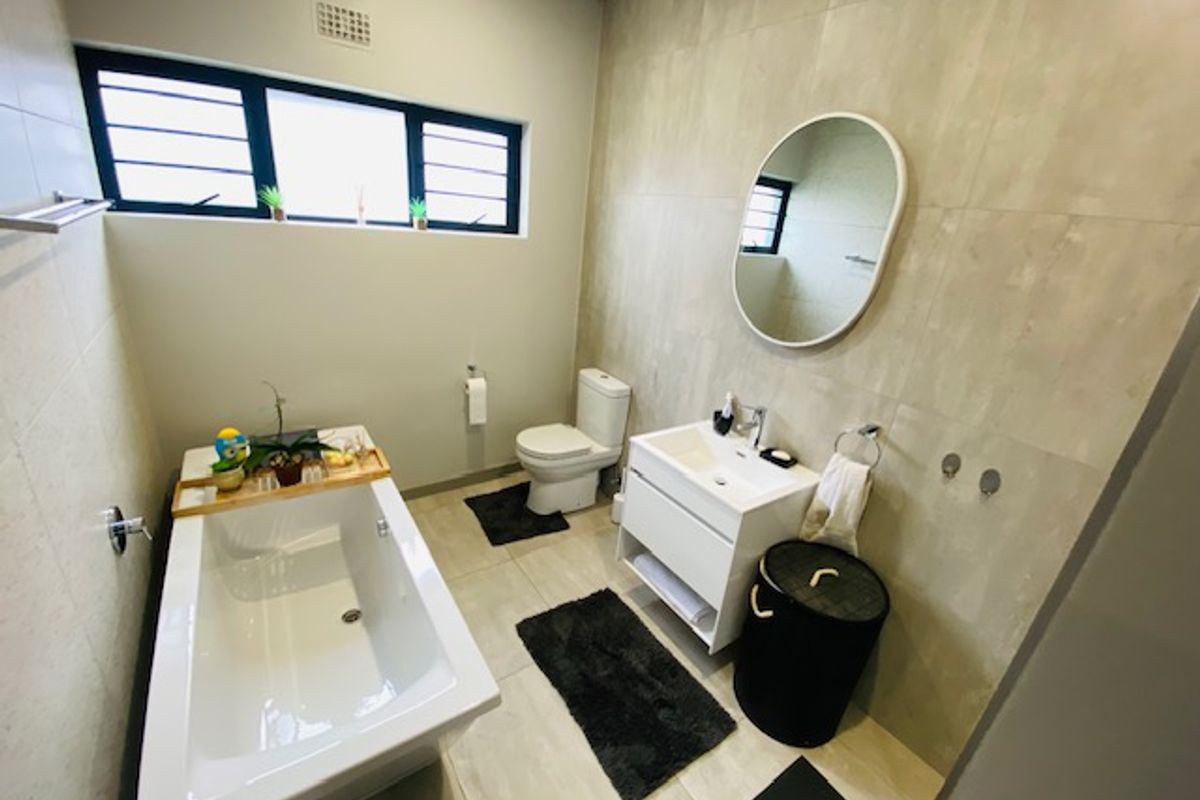 Modern bathroom featuring a sleek bathtub, wall-mounted vanity with basin, and neutral floor-to-ceiling tiling, creating a clean and functional space.